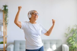 listening to music while you exercise provides many anti-aging benefits, older woman with headphones on dancing to the music